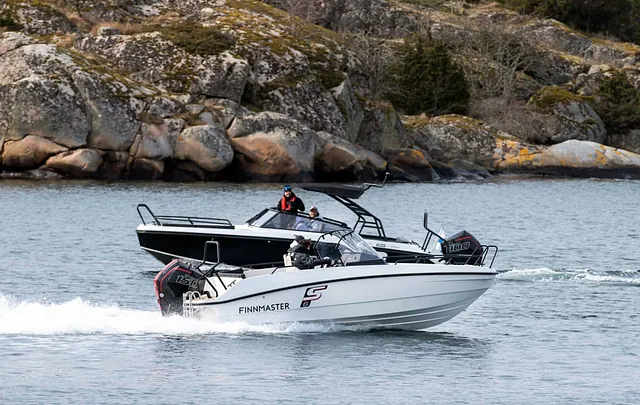 To motorbåter i fart på sjøen utenfor steinete kystlandskap, med personer om bord.