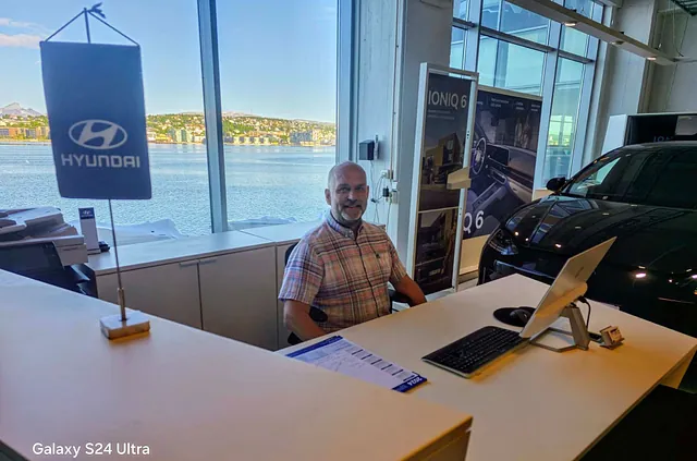Ansatt sitter bak kontorpult. Hyundai vimpel på bord.